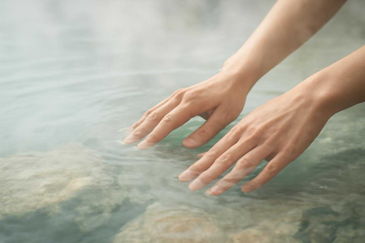 透き通った温泉のお湯に浸かる手と湯気の表現